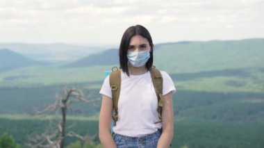 Bir dağın tepesinde duran koruyucu maskeli ciddi bir kızın portresi.