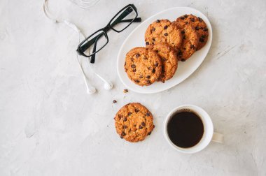 Amerikan çikolatalı kurabiye kahve gözlük ve kulaklık beyaz taş zemin üzerine beyaz tabak fincan. En iyi görünüm ve kopya alanı.