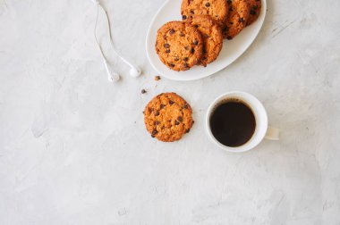 Kahve ve kulaklık beyaz taş zemin üzerine beyaz tabak fincan çikolatalı kurabiye. En iyi görünüm ve kopya alanı.