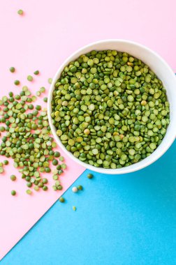 Çift tonlu arka plan üzerinde beyaz bir kase kuru pişmemiş yeşil bezelye. En iyi görünüm ve kopya alanı.