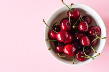 Hafif pembe bir arka plan üzerinde beyaz bir kase taze Olgun kırmızı kiraz yığını. En iyi görünüm ve kopya alanı. Organik gıda kavramı.