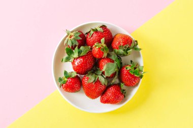 Çift tonlu arka plan üzerinde beyaz bir tabak içinde taze olgun çilek. En iyi görünüm ve kopya alanı. Organik gıda kavramı.