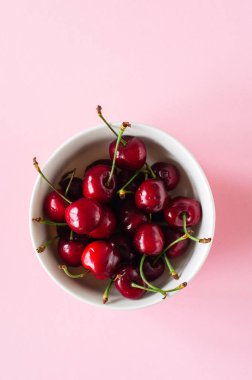 Pembe bir arka plan üzerinde beyaz bir kase taze Olgun kırmızı kiraz yığını. En iyi görünüm ve kopya alanı. Organik gıda kavramı.