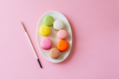 Renkli macarons - pembe bir arka plan üzerinde beyaz bir tabak kurabiye Fransız. En iyi görünüm ve kopya alanı.