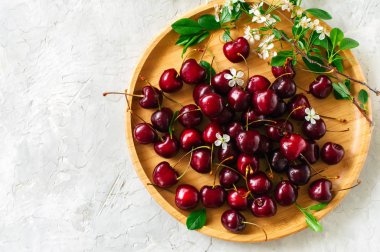 Taze olgun kiraz ahşap bir tabak içinde. Beyaz taş zemin. Üstten görünüm. 