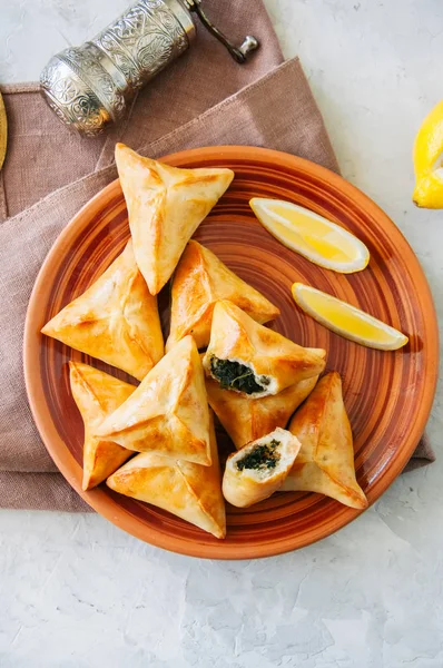 Arabic and middle eastern food concept. Fatayer sabanekh - traditional arabic spinach triangle hand pies  on a white stone background.
