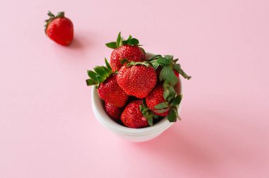 Pembe bir arka plan üzerinde beyaz bir kase üzerinde taze olgun çilek. Uzay kopyalayın. Üstten görünüm.