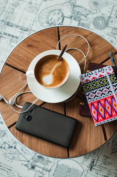 Cup of coffee notebook, smartphone and headphoes on a table. Flat lay, life style Top view.