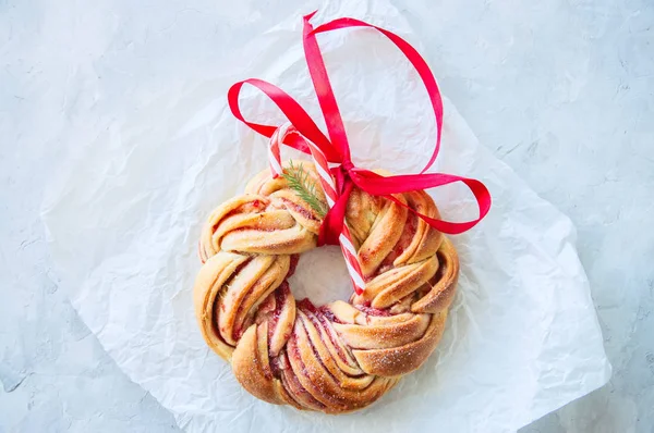 Raspberry jam swirl brioche wreath with candy cane and red ribbon on a baking paper