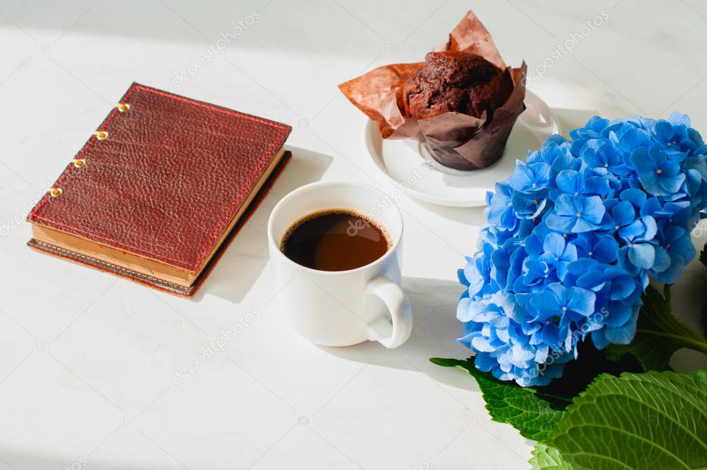 A cup of coffee, chocolate muffin, hydrangea and notebook on a white background. Overhead view.
