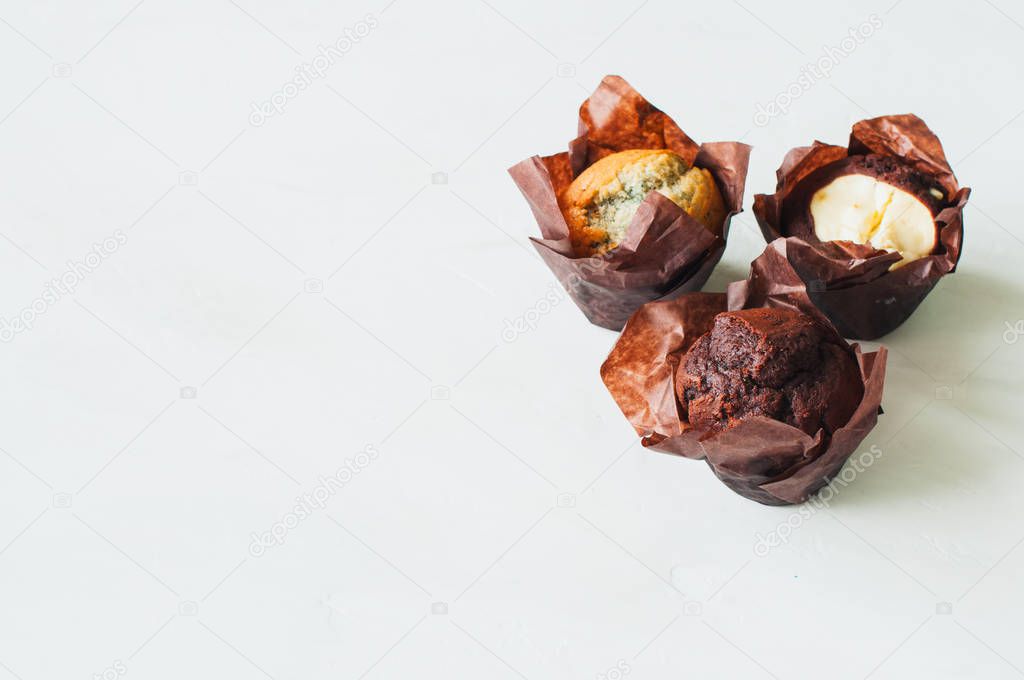 Three different muffins on a white background. Chocolate, bluberry and brownie cheesecake muffins. Copy space.