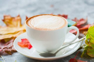 Akçaağaç yaprakları ile gri bir arka plan üzerinde kapuçino bir fincan