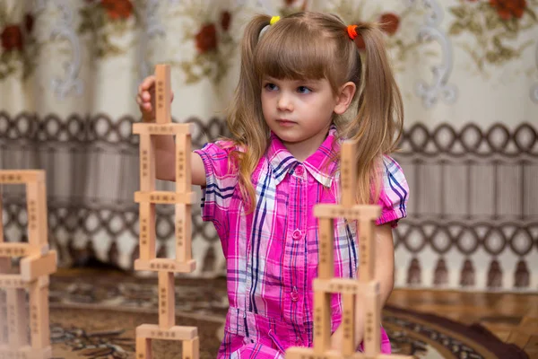 Little girl play with wooden blocks. Kid inspecting wooden block buildings, childhood activities. Tower stack from wooden blocks toy and girl\'s hand take one block