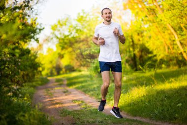 Günbatımı ve dinle müzik Park koşan atletik genç adam. Sağlıklı yaşam tarzı