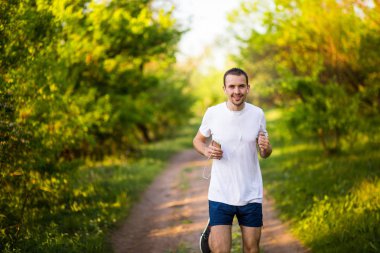 Günbatımı ve dinle müzik Park koşan atletik genç adam. Sağlıklı yaşam tarzı