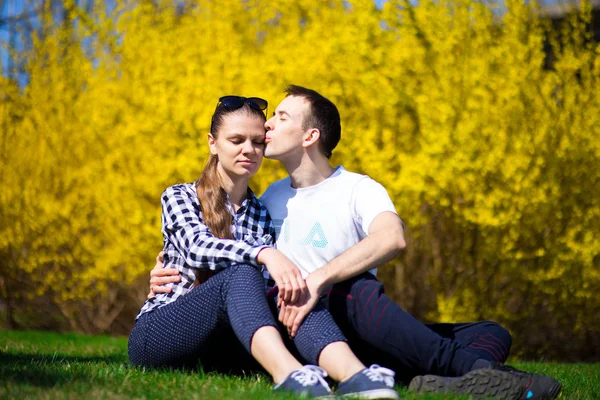 Couple in love hug in park on fresh green grass near tree in yellow blossom. Summer time