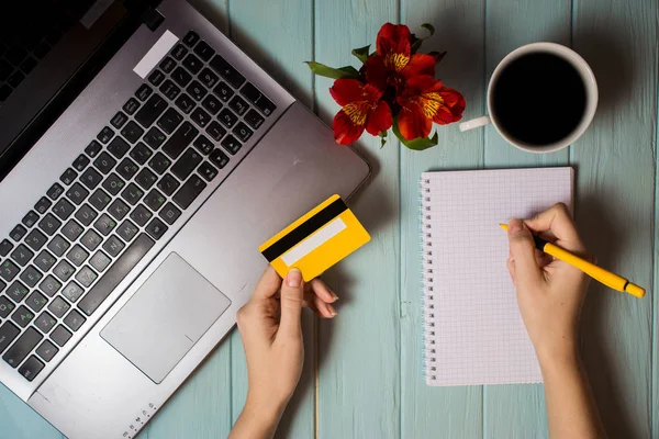 Woman's hand holds credit card over table, online shopping gifts through phone during coffee break. Concept of new technology. Flat lay