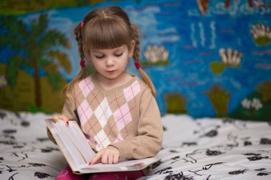 Küçük neşeli kız yatakta kitap okuyun. Çocuklar bilgi kavramı