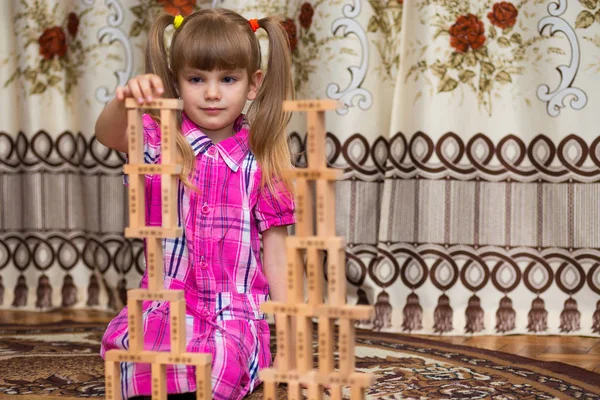 Little girl play with wooden blocks. Kid inspecting wooden block buildings, childhood activities. Tower stack from wooden blocks toy and girl\'s hand take one block