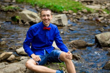 Yakışıklı orman Nehri yakınında mavi gömlek gülümseyen genç portresi. Duygular kavramı