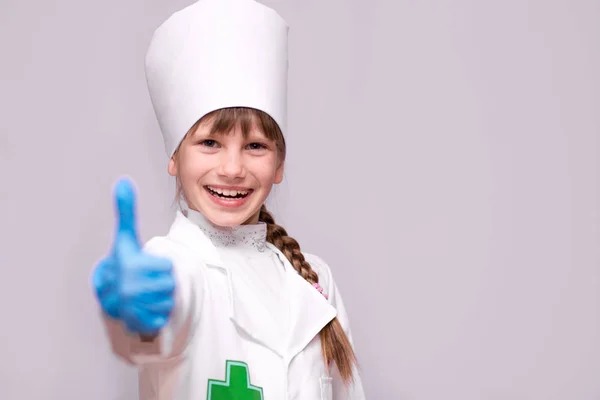制服と青の医療用手袋の幸せな小さな女の子医師が親指を現す — ストック写真