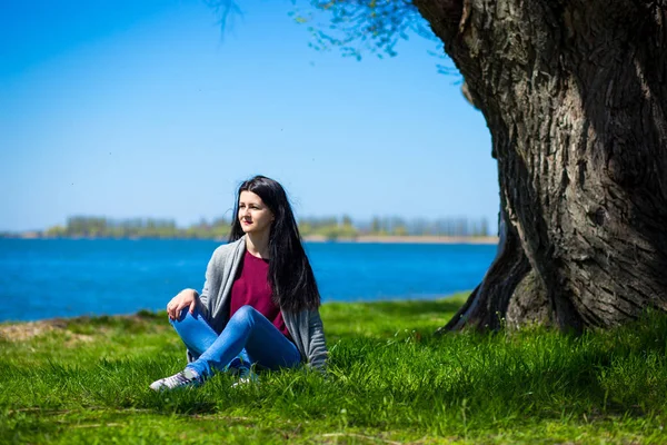 Mooie Jonge Vrouw Jeans Zit Oever Van Rivier Buurt Van — Stockfoto