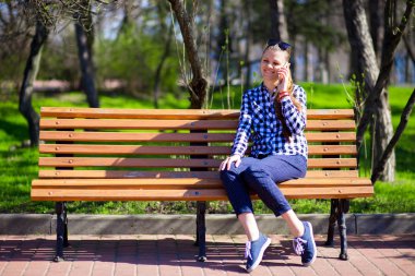 Parktaki bankta otururken cep telefonu kullanan genç bir kadın.