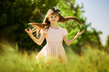 Portrait of beautiful little girl in elegant dress in middle of green summer field clipart