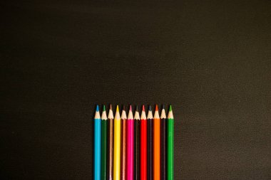 Collection of colored pencils on black chalkboard background clipart