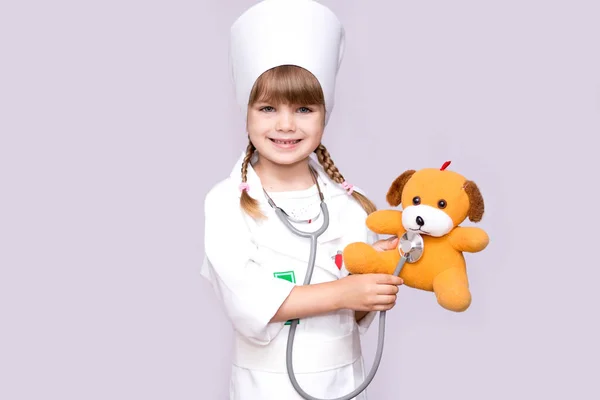 Smiling little girl playing doctor and listening teddy bear with stethoscope isolated on white