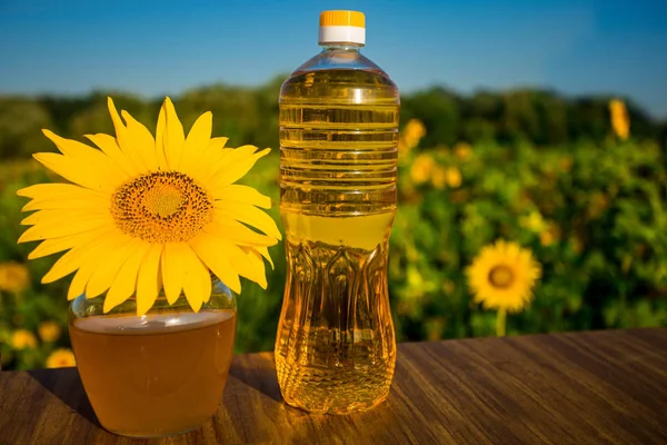 Glass honey jar and bottle of oil on wooden stand with sunflowers field background. Photo with copy space area for text