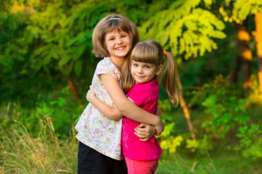 İki sevimli küçük gülüyor ve güneşli günde yaz parkta sarılma kız