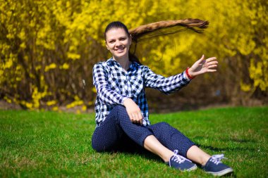 Genç kız sarı çiçek ağacında yakınındaki taze yeşil çimenlerin üzerinde Park'ta rahatlayın. Yaz saati