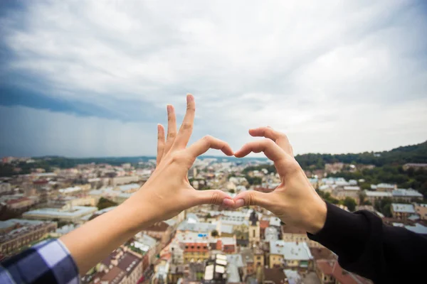 Couple hands in form of heart against old european city. Hands in shape of love heart with dramatic sky