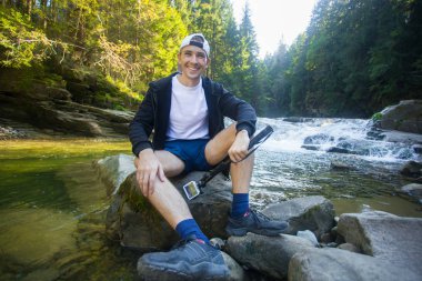 Ormanın ortasında hızlı Nehri yakınında eylem kamera yürüyüş ile genç adam