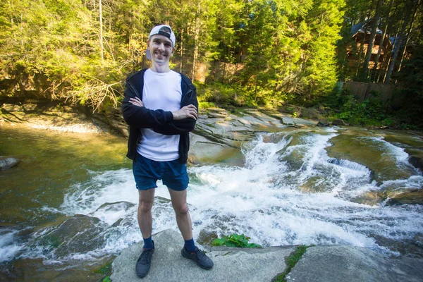 Young man walk near fast river in middle of forest