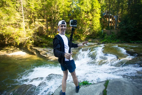 Young man with action camera walk near fast river in middle of forest