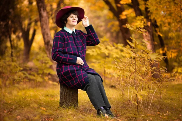 60 year old woman in red hat dreams in gold autumn par