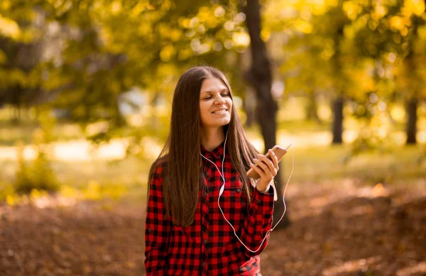Ładna Dziewczyna Gospodarstwa Telefon Słuchania Muzyki Jej Słuchawki Jesienny Park — Zdjęcie stockowe