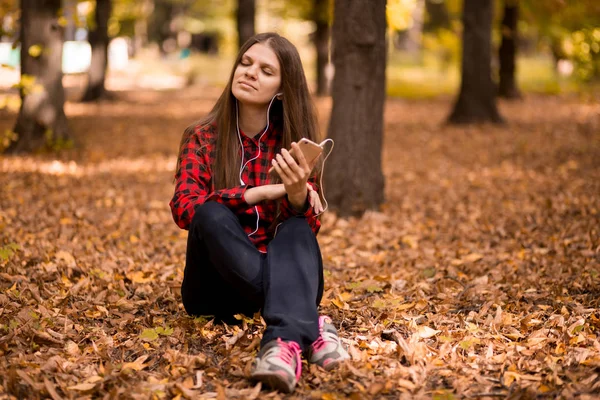 Ładna Dziewczyna Gospodarstwa Telefon Słuchania Muzyki Jej Słuchawki Jesienny Park — Zdjęcie stockowe