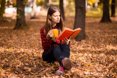 Kadın sonbahar park kitap ve sıcak bir içecek ile fincan elinde tutan