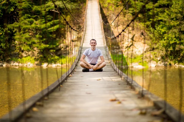 Young happy man on bridge over river in autumn nature with mountains