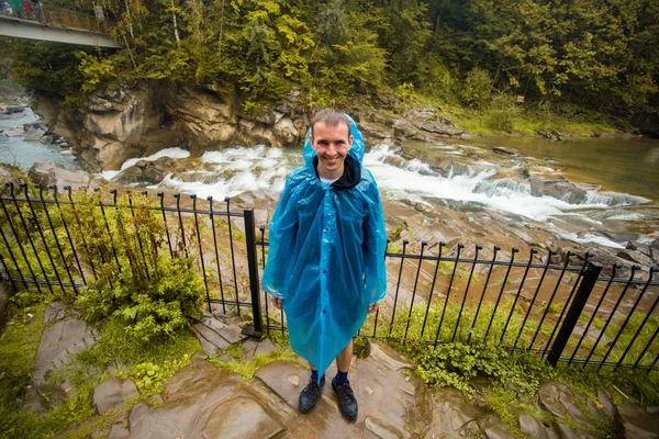 Young man in blue raincoat stands in rain