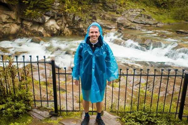 Young man in blue raincoat stands in rain