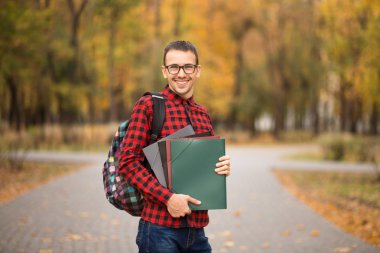 Kendine güvenen öğrenci. Sırt çantası klasörlerle sonbahar park holding yakışıklı genç adam portresi