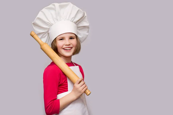 Children cook. Happy little girl in chef uniform holds rolling pin isolated on white background. Kid chef.