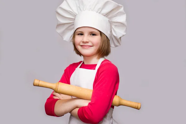 Children cook. Happy little girl in chef uniform holds rolling pin isolated on white background. Kid chef.