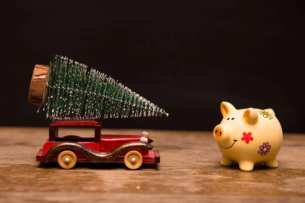 Piggy bank and toy car with christmas tree on wood over dark rustic background with copy space for text