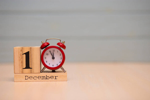 December 1st set on wooden calendar and red alarm clock with blue background. Clock face showing five minutes to midnight