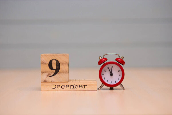 December 9th set on wooden calendar and red alarm clock with blue background. Clock face showing five minutes to midnight